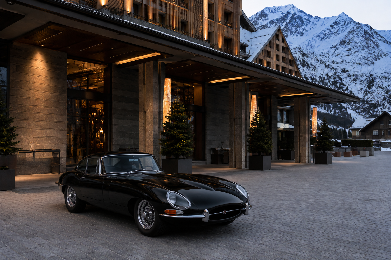 Luxury alpine hotel entrance at dusk with a classic black Jaguar E-Type and snow-capped mountains