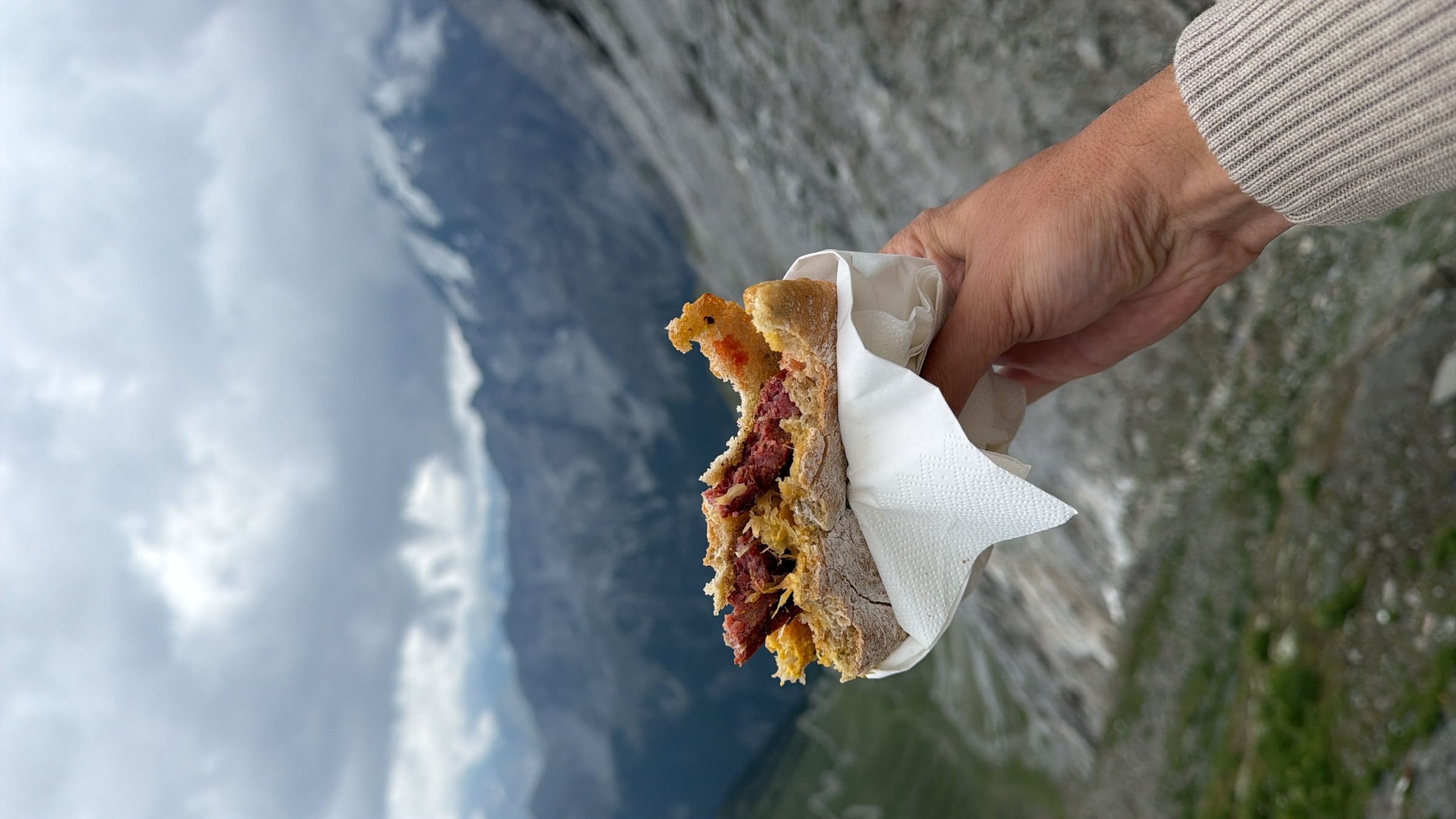 A sandwich with venison sausage and sauerkraut, held up against the view from the Stelvio summit